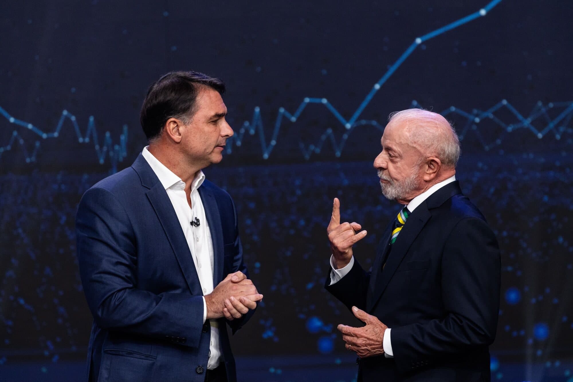 Flavio Bolsonaro and Luiz Inacio Lula da Silva face each other in conversation on a debate stage