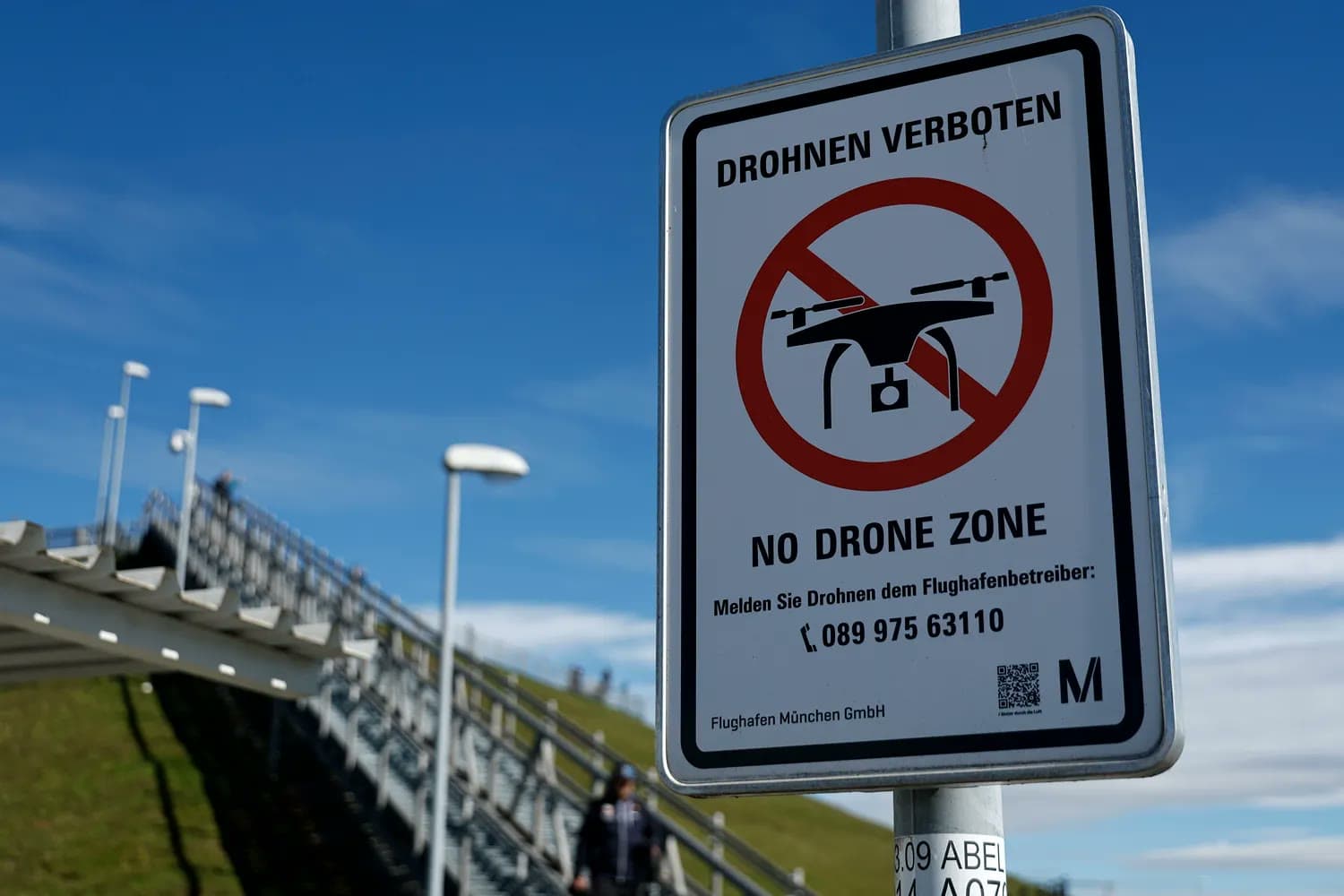 A 'No Drone Zone' warning sign in German and English posted near an airport walkway in Germany.
