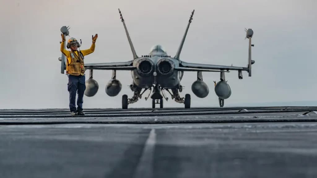 A U.S. Navy flight deck crew member directs an F/A-18 fighter jet on an aircraft carrier deck