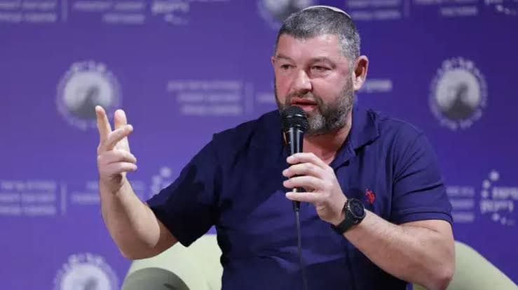 Ofer Winter speaking into a microphone while gesturing, seated on a panel stage