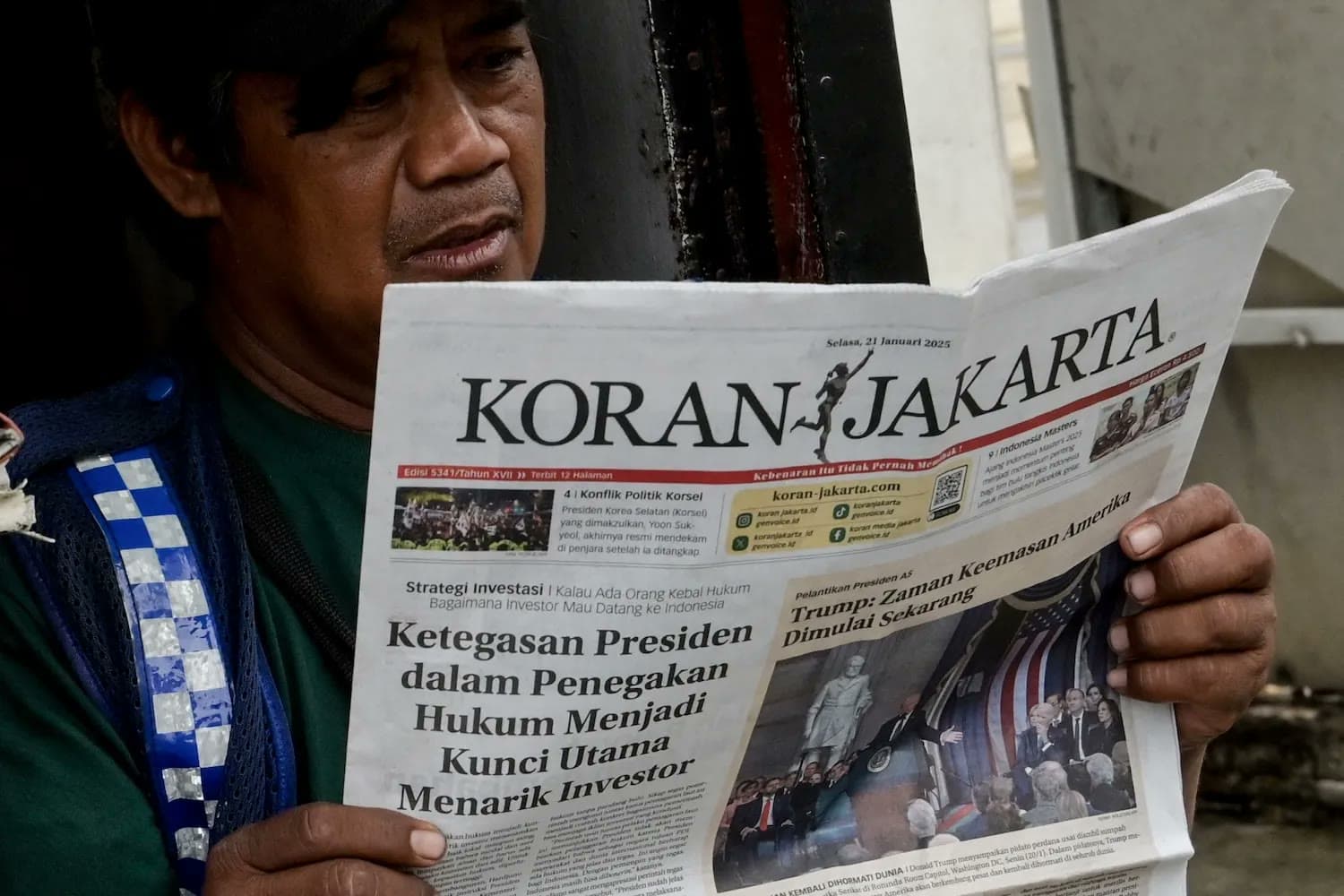 A man reads a copy of the Indonesian newspaper Koran Jakarta with a front-page photo of Donald Trump's inauguration.