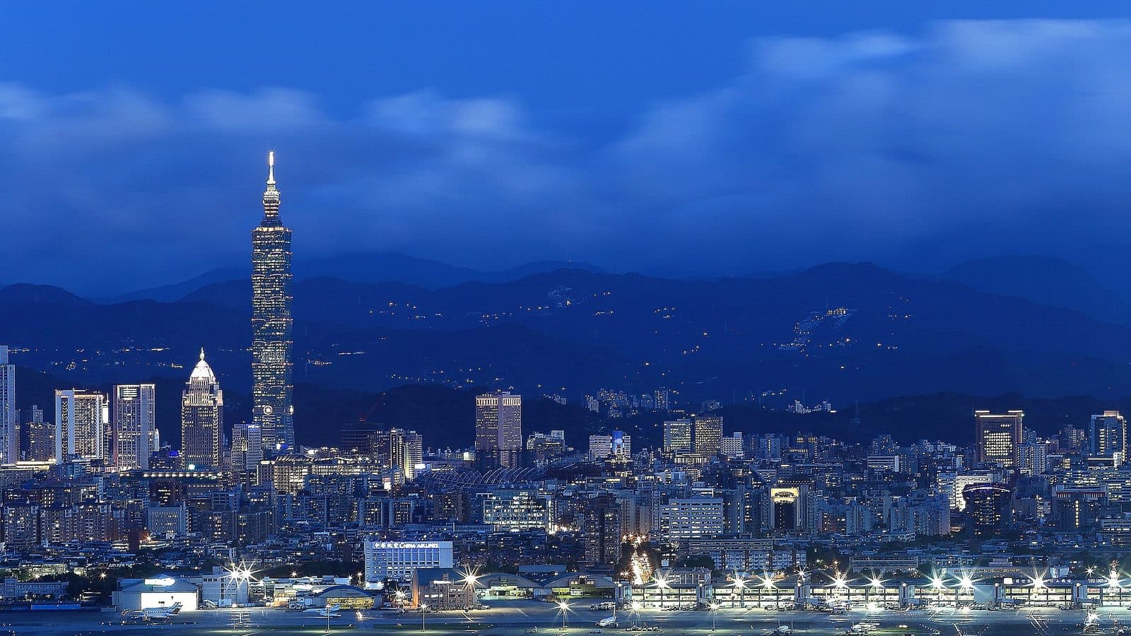 Nighttime skyline of Taipei, Taiwan, with Taipei 101 lit up against surrounding mountains