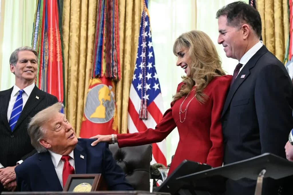 President Trump seated at the Resolute Desk in the Oval Office surrounded by officials during a signing event