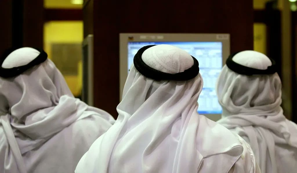 Three men in traditional Gulf dress watch a stock market screen displaying trading data.