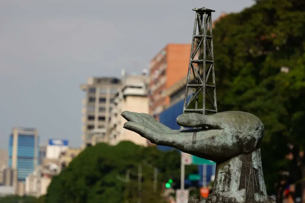 A bronze statue of a hand holding a small oil derrick against a city skyline in Venezuela.