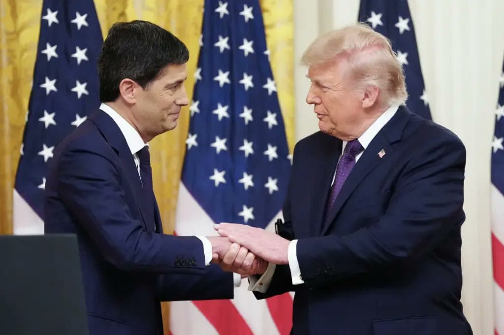 Kevin Warsh and Donald Trump shake hands facing each other at a White House event, American flags in the background.